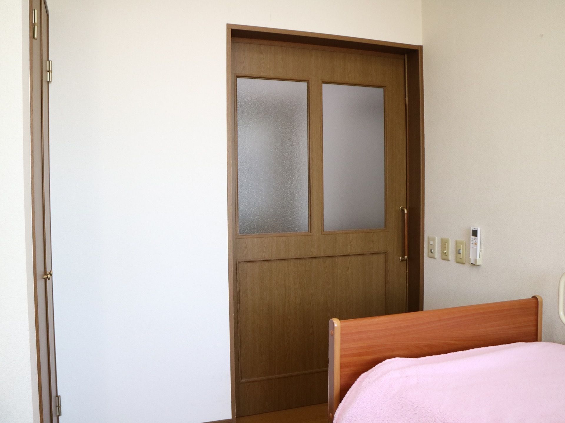 居室入口はすりガラスが入った引き戸になっている。入口近くにエアコンのリモコンや照明器具のスイッチがある。