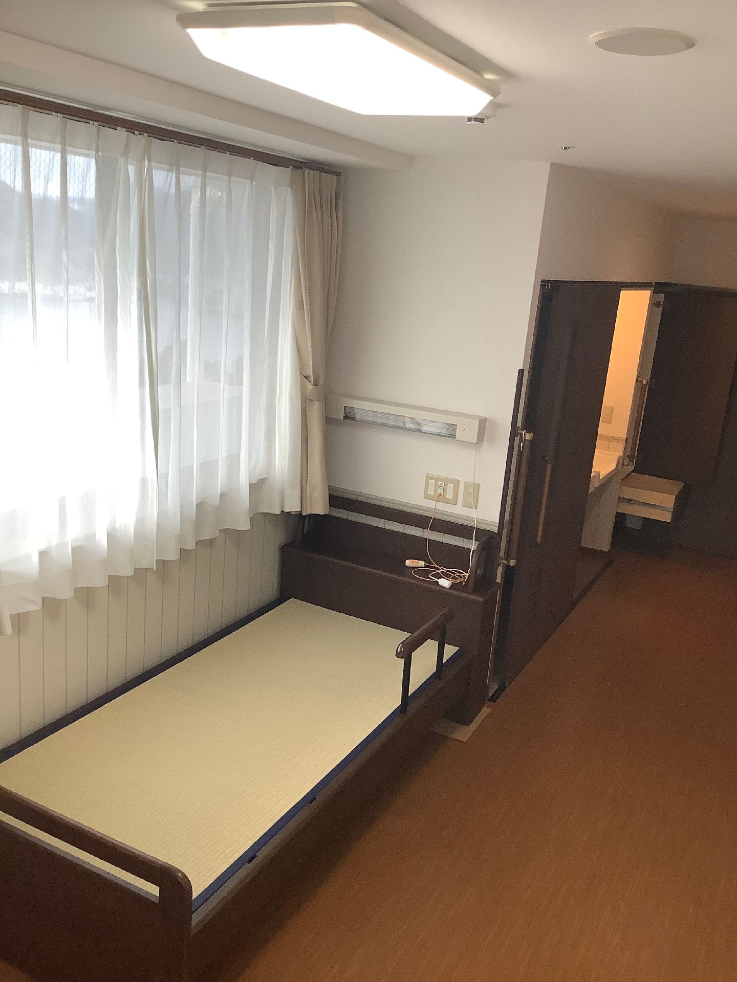 介護ベッドの頭に近い部分に緊急通報装置が付いている。奥にはトイレも設置されている。