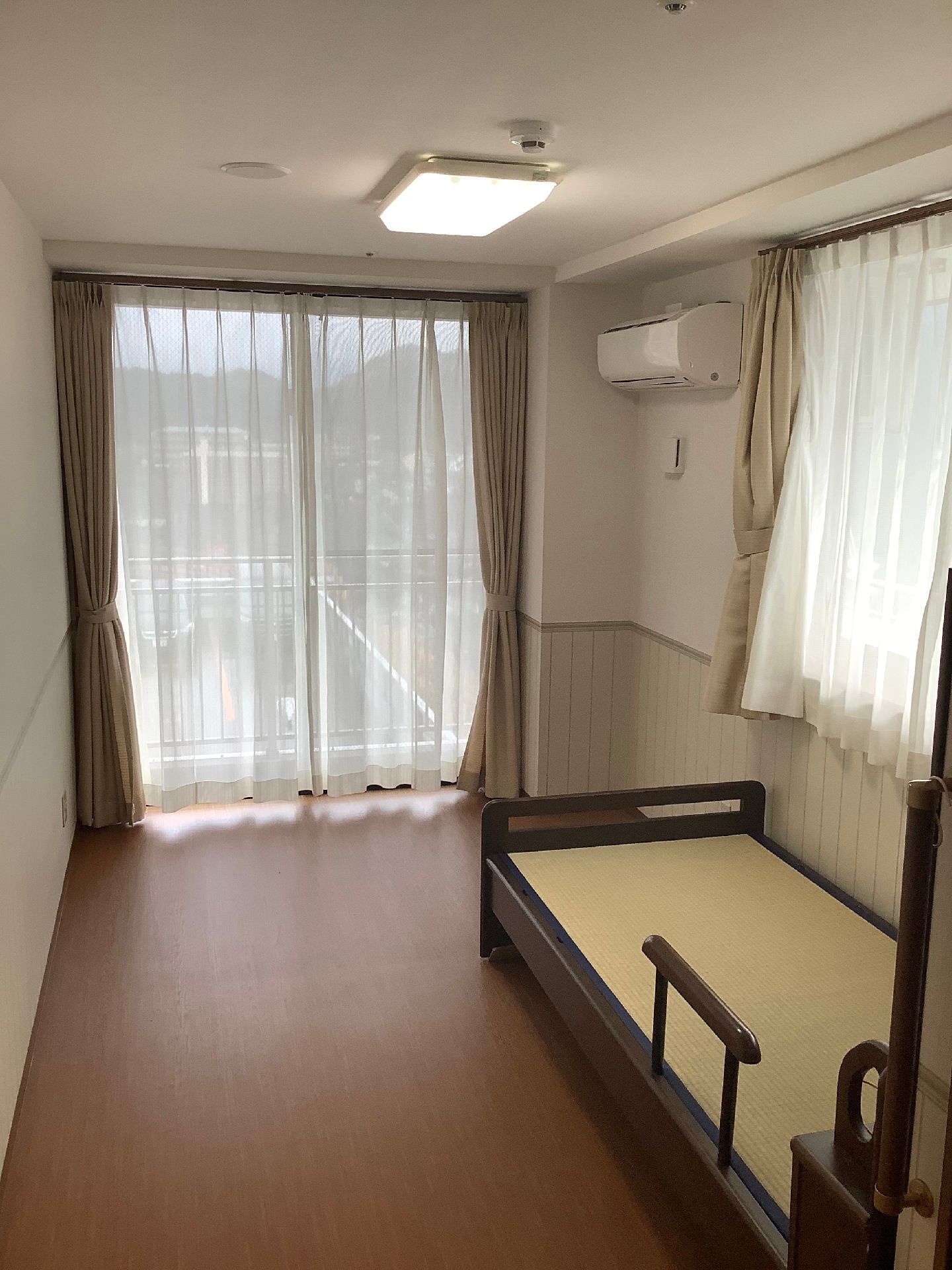 エアコンが付いた部屋には二つの窓があり、カーテンが付いている。介護ベッドもある。