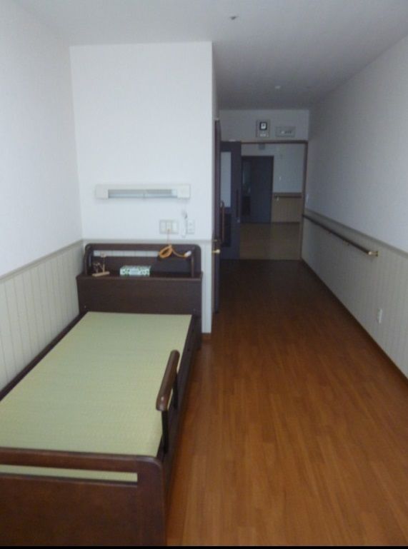介護ベッドが置かれたフローリングの部屋の壁には手すりが設置され、ベッドサイドには緊急通報装置がある。