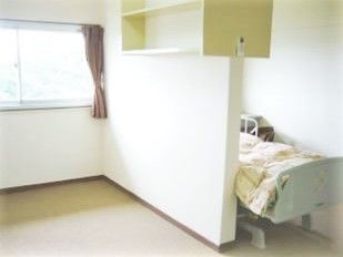 介護用ベッドと小さな机といす、エアコンが置いてある小さなワンルームの様子