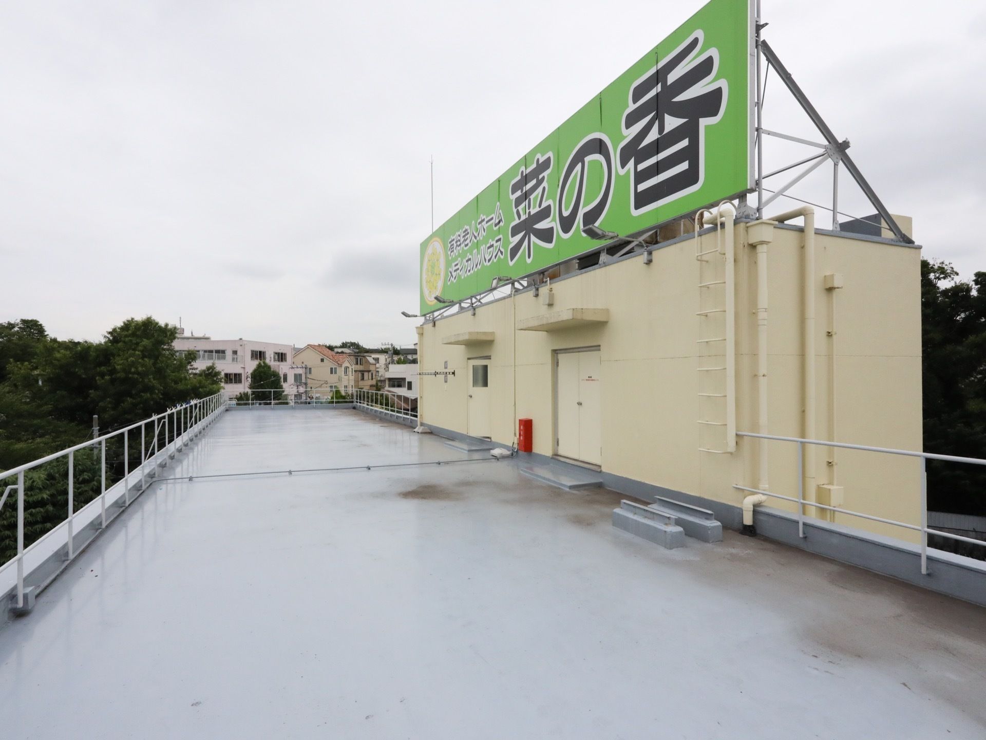 屋上に施設名が書かれた大きな看板が設置されている。周辺には豊かな緑と住宅街が広がっているのが見える。
