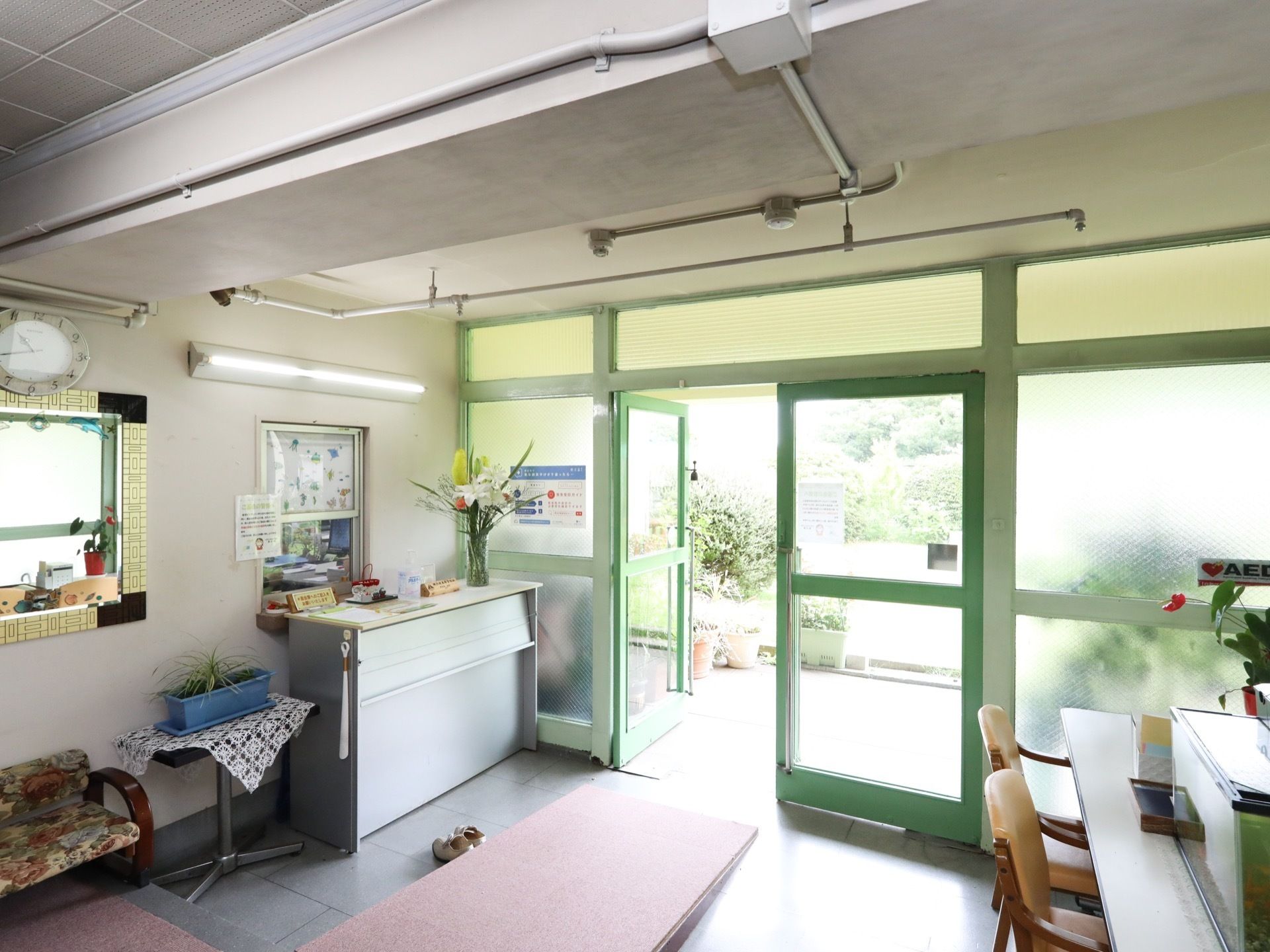 受付が設けられているエントランスホールで、施設入口はガラス張りで両開きとなっている。カウンターの上に花が飾られている。