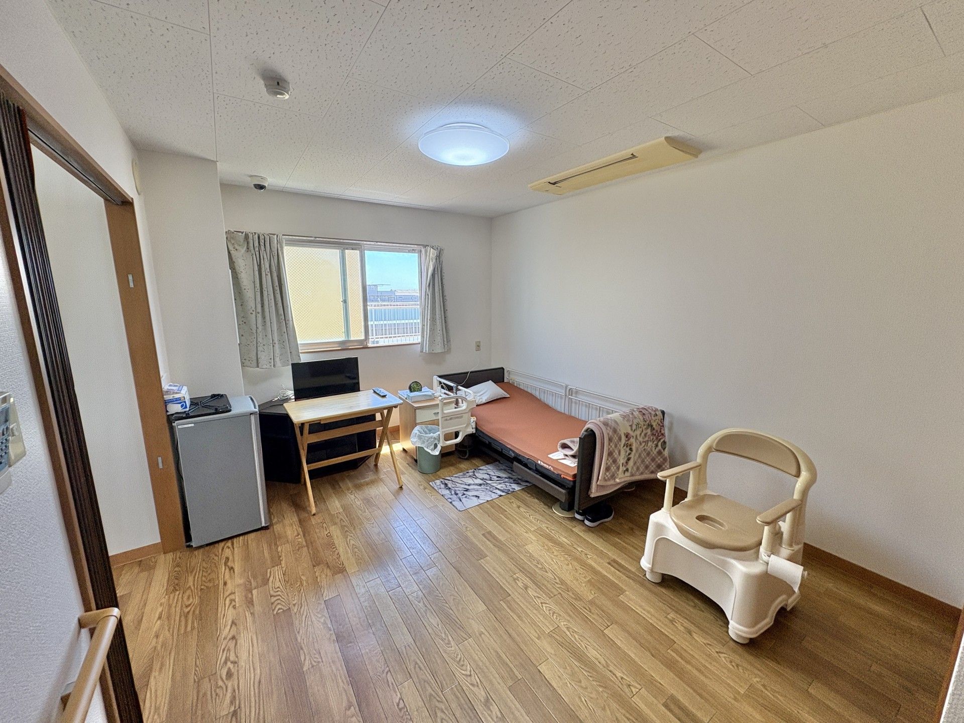 屋外でチェックのシャツを着た高齢男性が車いすに座り、そばにいるポロシャツを着た女性スタッフと話している。