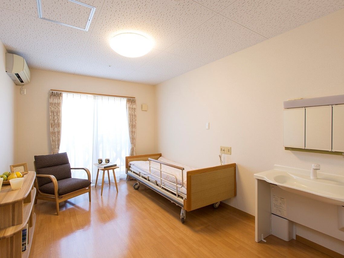 高齢女性が座って赤いロープを両手で引っ張っている様子。すぐそばには若い男性スタッフが座り、女性の手を握ってサポートしている。