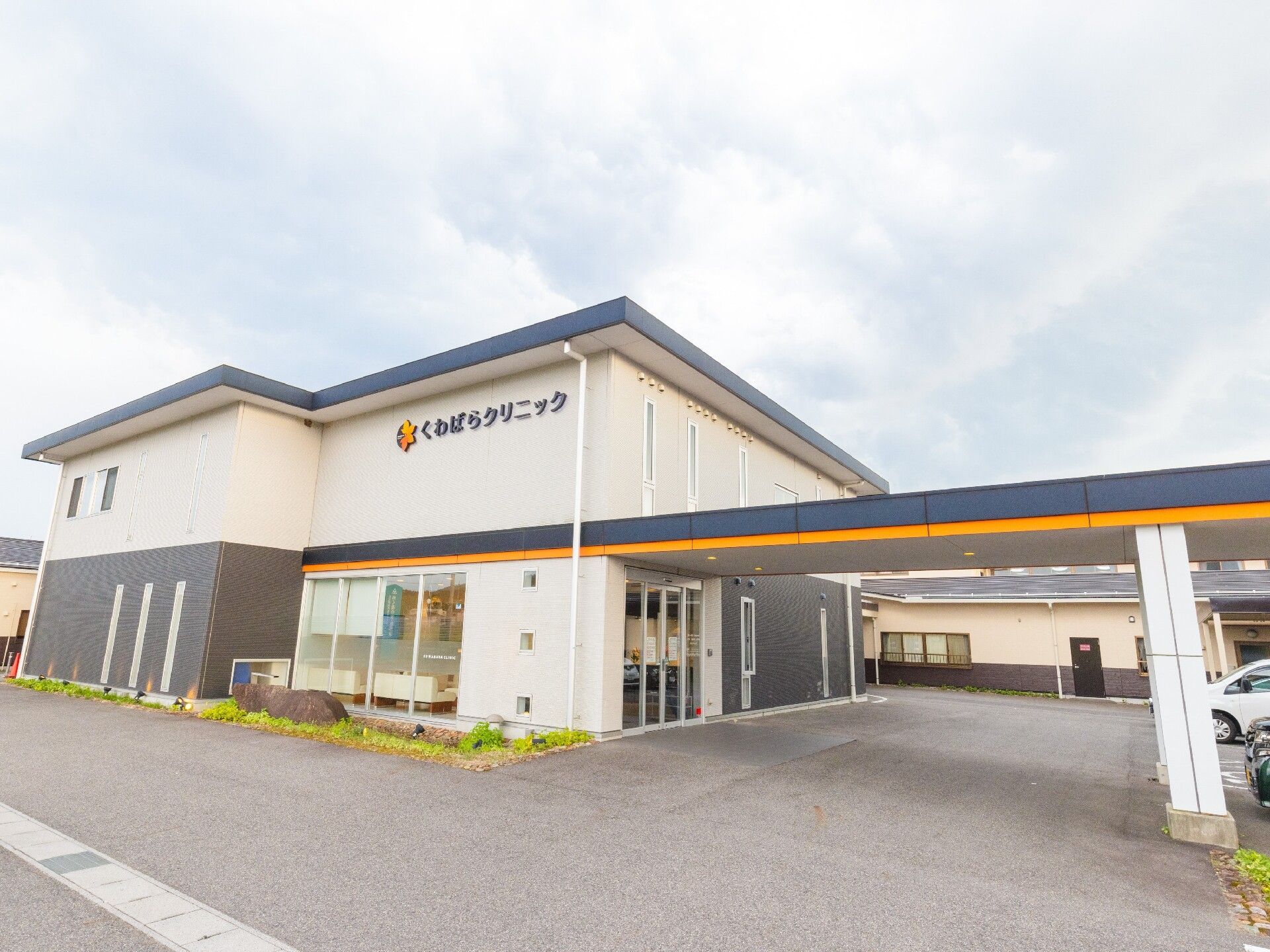 ボーダー柄のエプロンを付けた女性スタッフが白いシャツを着た高齢男性を介助している様子。スタッフは男性に笑いかけている。