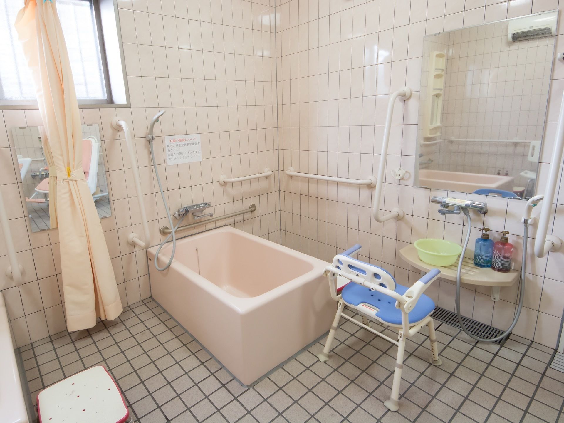 白を基調としたタイル張りの浴室で、上部に窓が設置されている。シャワーチェアや桶、シャンプーなどが用意されている。