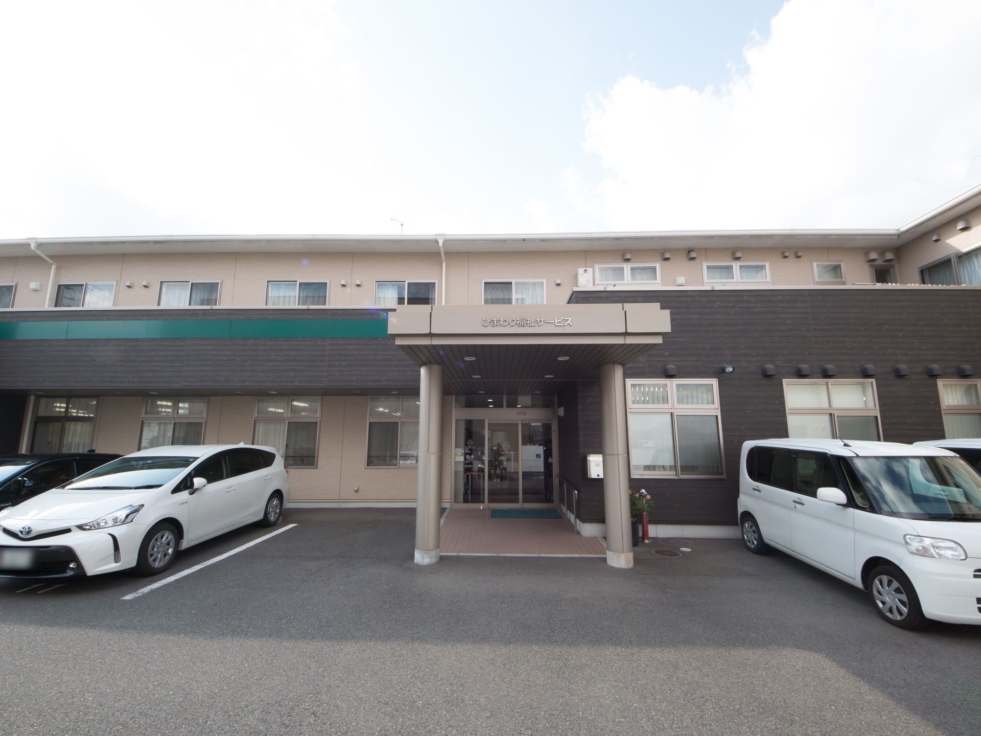 ２階建ての落ち着いた色合いのグループホームである。玄関は自動ドアとなっており、横には手すりが設置されている。