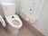 清潔感あふれる個室トイレである。温水洗浄機能付きの便座で、壁には手すりや呼び出しボタンが設置されている。