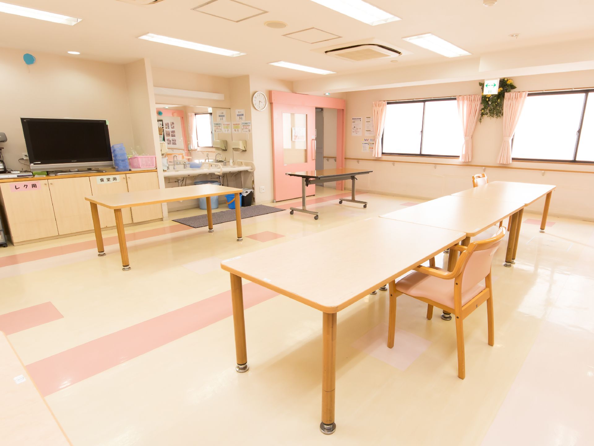 白とピンクベースの、明るく広々とした共有スペースである。大きなテーブルに洗面台、テレビ、サイドボードなどが備わっている。
