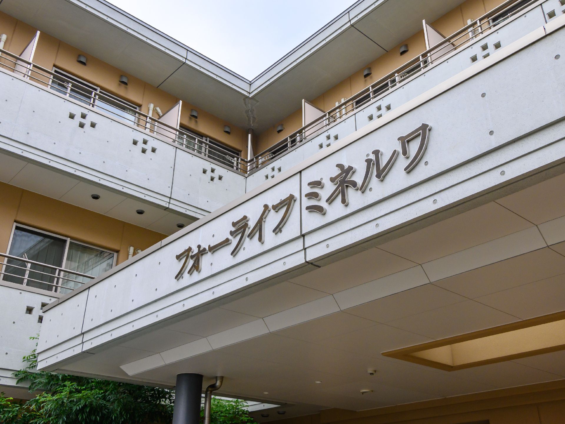 ピンクのカーディガンを着た高齢女性がエプロンを付けた女性スタッフと一緒に並んで笑っている。