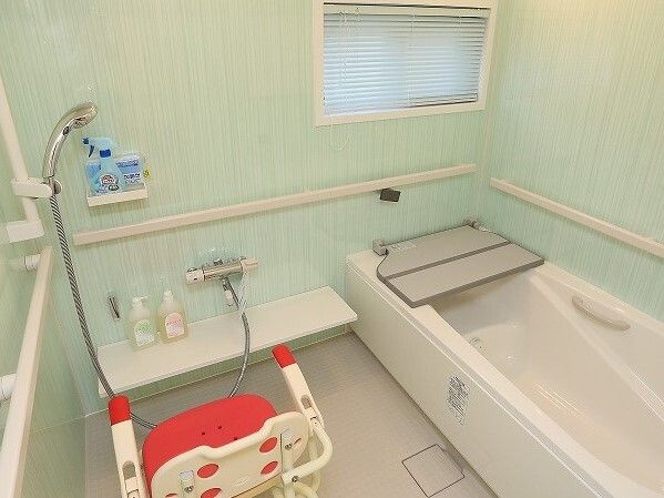 ミントグリーンの浴室には白い一人用の浴槽があり、浴槽には折り畳みのベンチが付き、シャワーの前にはシャワーチェアがある。