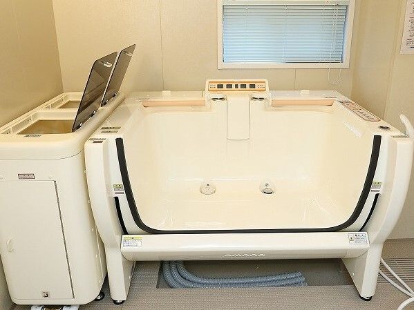 分別用のゴミ箱のような形のタンクが付いた機械浴。浴槽の一面の壁がなく、ボタンで操作するようになっていて、したにはホースがある。