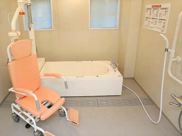 ピンクのリフトが天井からつるされている浴室。奥には白い浴槽が設置され、右手にはシャワーがあり、洗い場が広い。