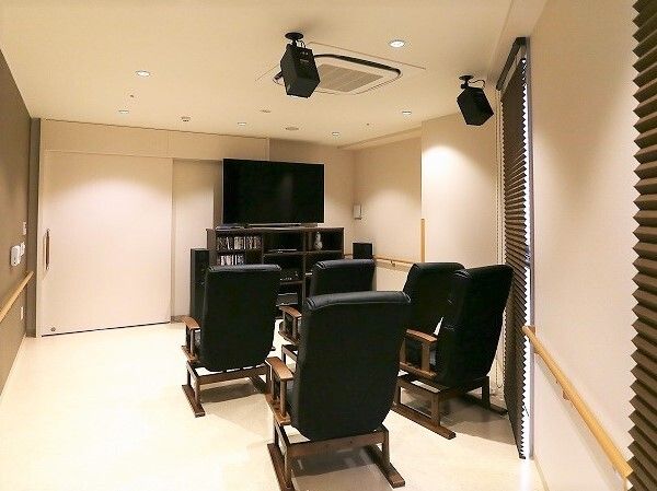 大きなテレビや音響システムが設置された部屋。ロッキングチェアのようなデザインのゆったりとした黒い椅子が並んでいる。