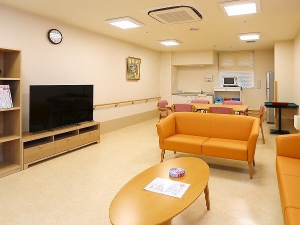 手前にはテレビや楕円形のローテーブル、オレンジのソファなどが置かれ、奥にはダイニングテーブルとキッチンがある。
