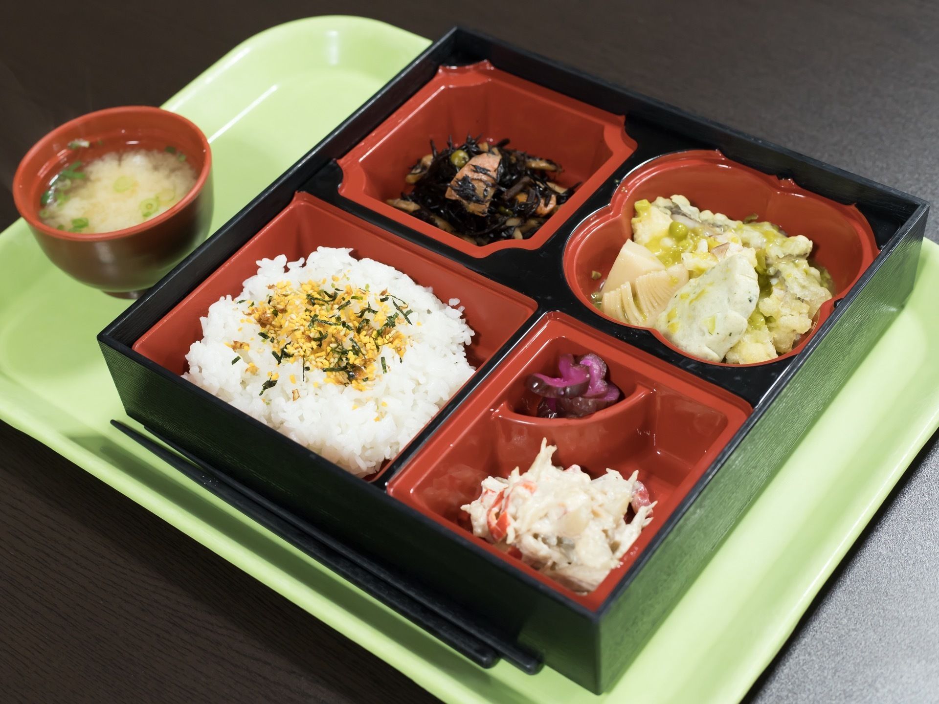 食事の一例。緑色のトレーの上に、ご飯やおかずが盛られたお弁当とお椀に入れられたみそ汁が並べられている。