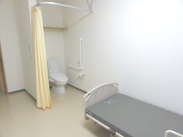 ドアレスタイプのトイレとベッドが置いてある空間。小さなワンルームタイプの部屋