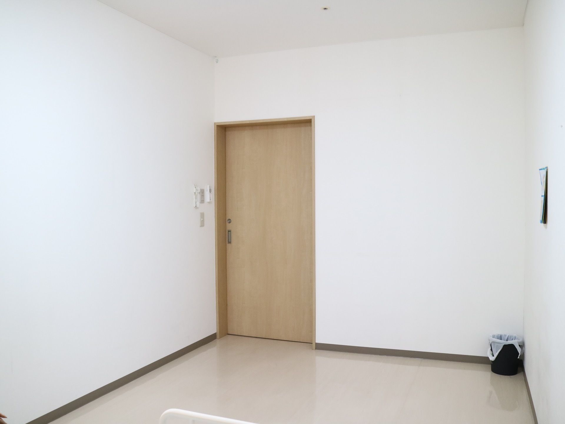 木製で施錠可能なドアになっている。壁にはカレンダーが掛けられており、部屋の隅には小さなゴミ箱が置かれている。