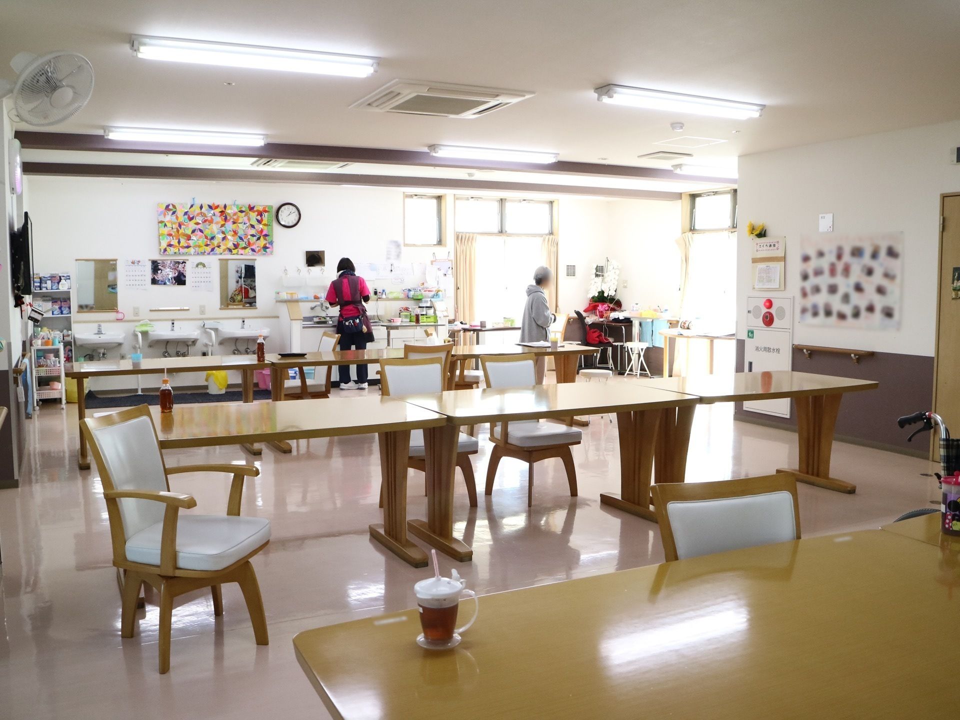 三つの洗面台と小さなキッチンがあり、テーブルが並べられている食堂