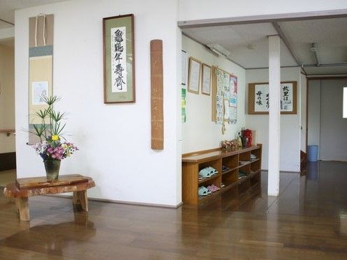 濃い色合いのフローリング仕様の床が印象的な施設内。掛け軸や和風の生け花がある静謐な雰囲気がある場所