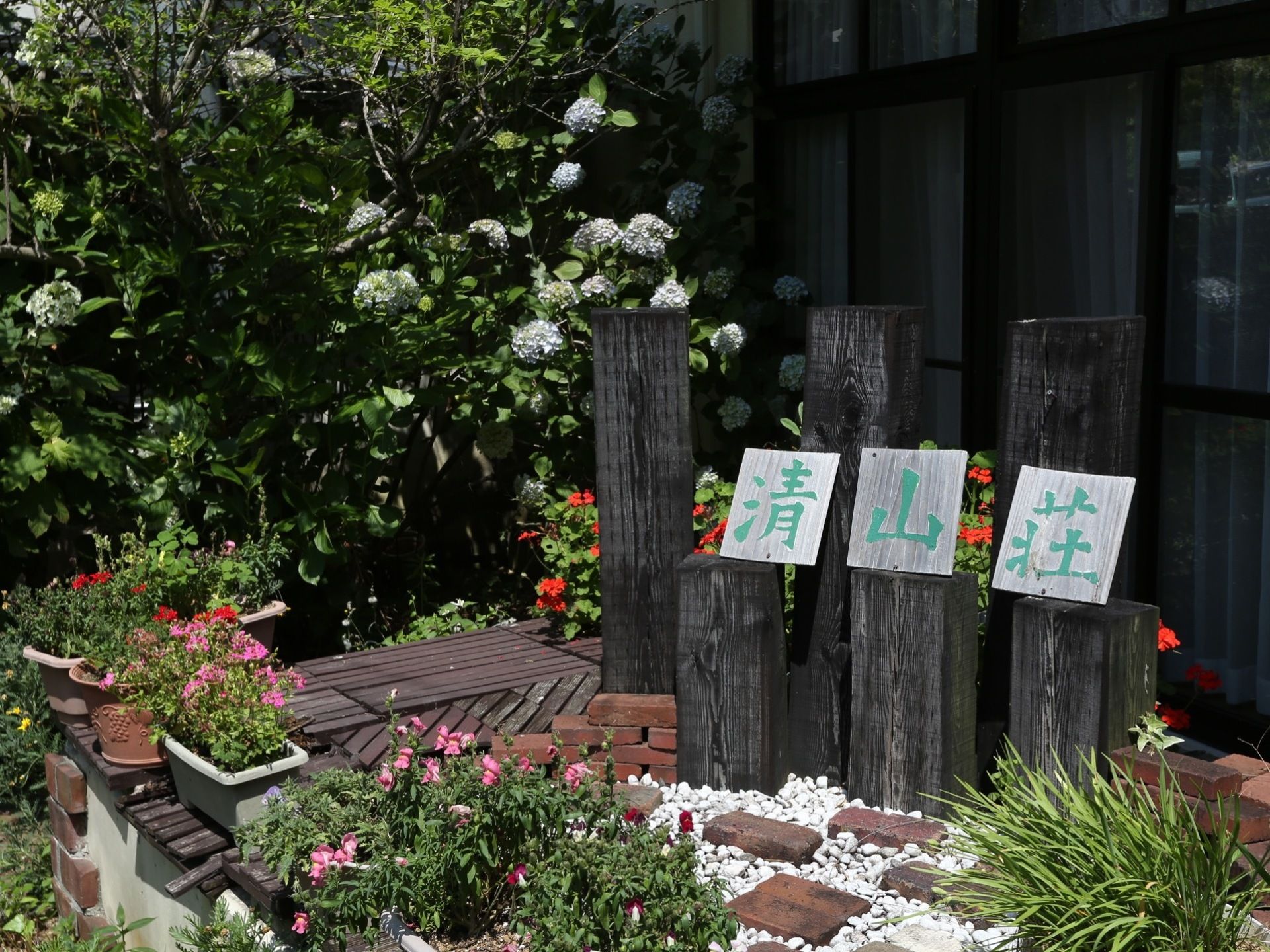 施設前に設置されている看板。黒く加工された木材をふんだんに利用し、周囲には観葉植物の鉢植えなどをあしらっている。