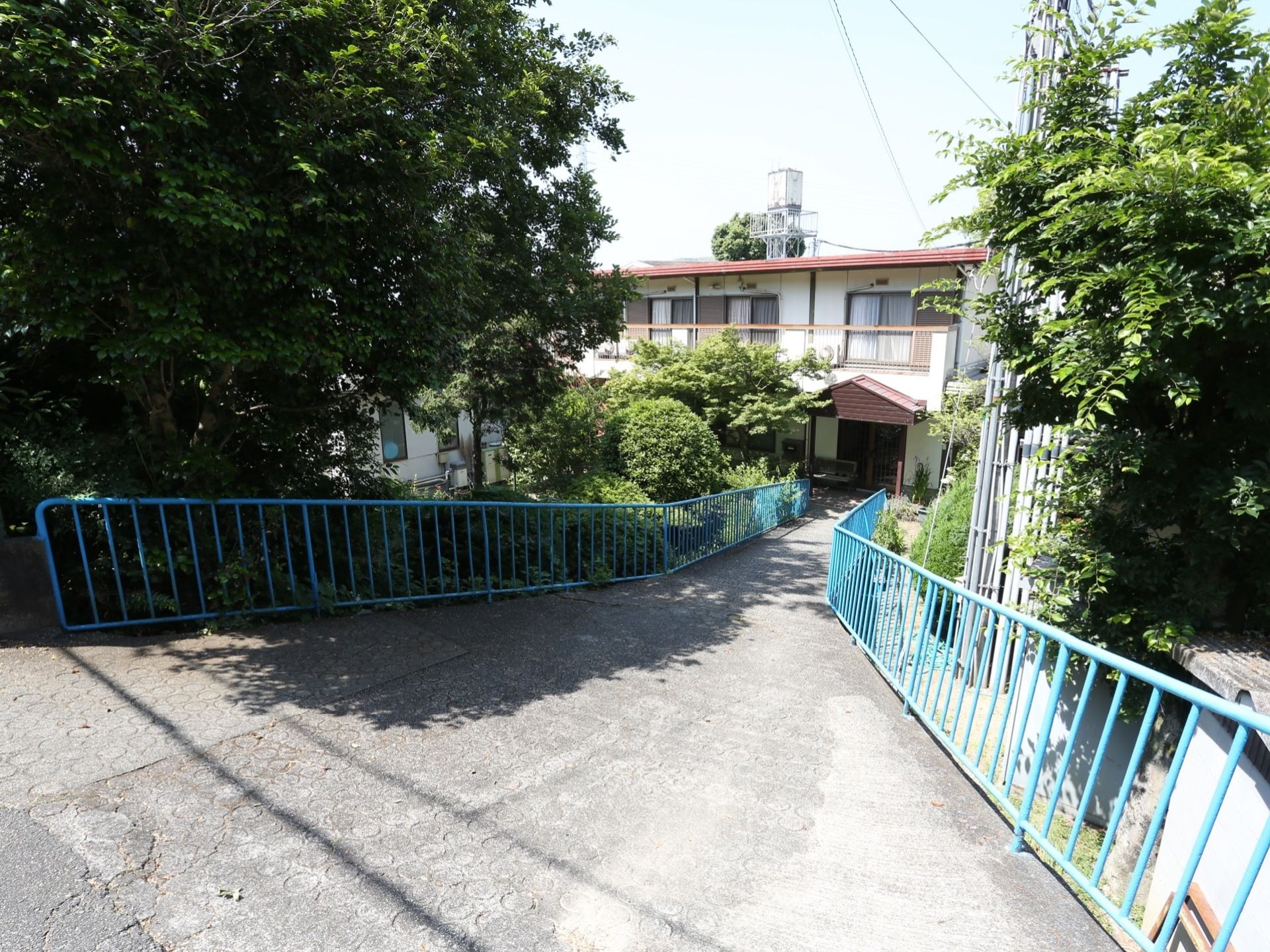 きれいに舗装された通路が、建物の入り口に続く。通路の両側には鉄柵があり、奥には樹木がうっそうと茂っている。