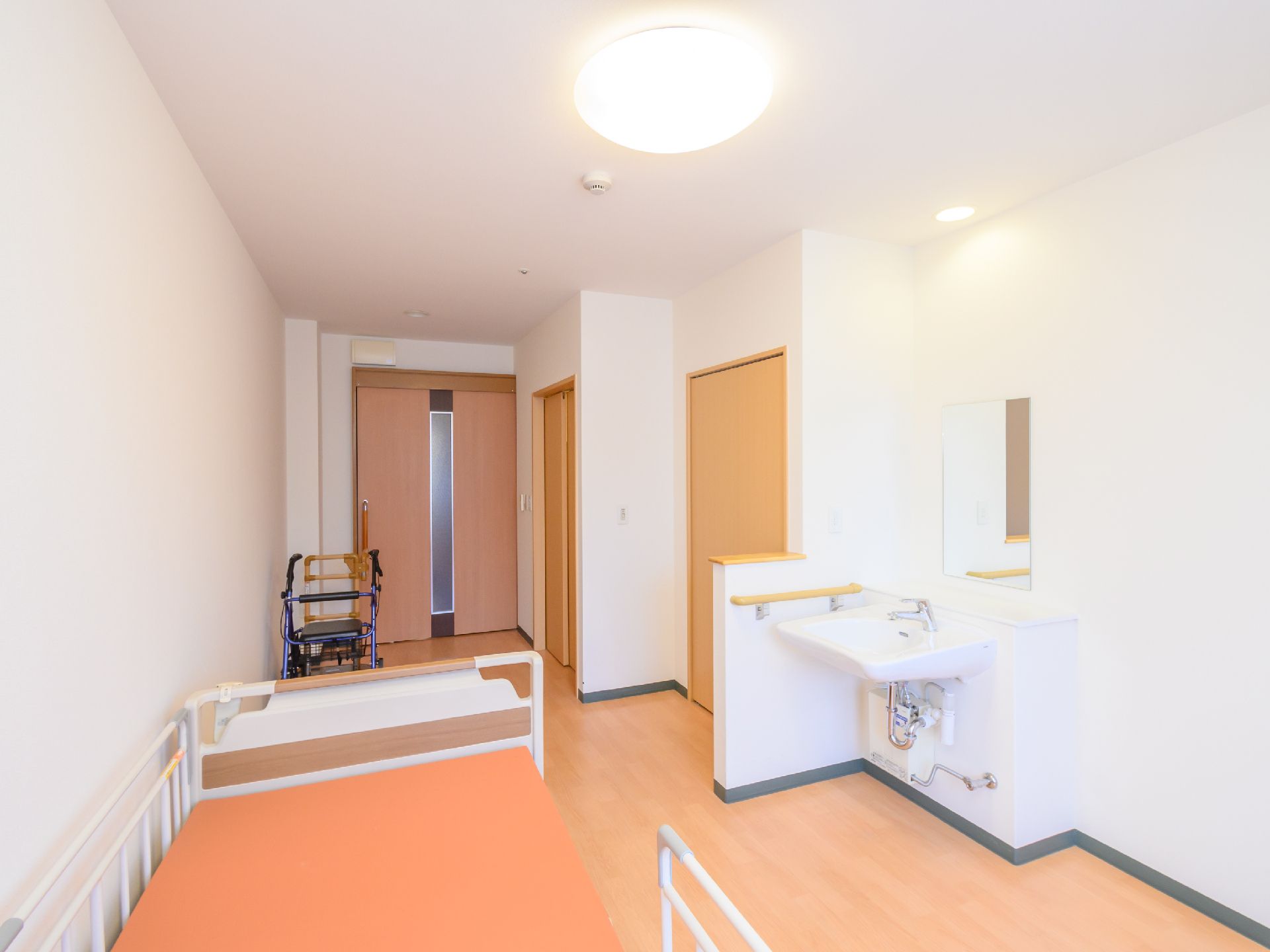 オレンジ色のマットレスが敷かれたベッドと洗面台が置かれた白い壁の部屋