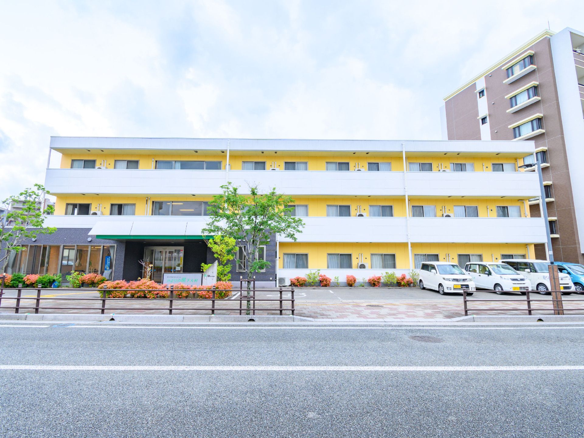 道路の奥に立地している黄色と白の外観の３階建ての建物