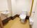 広いトイレには洋式便器とエル字型の手すり、オレンジ色の呼び出しボタンが設置されている。