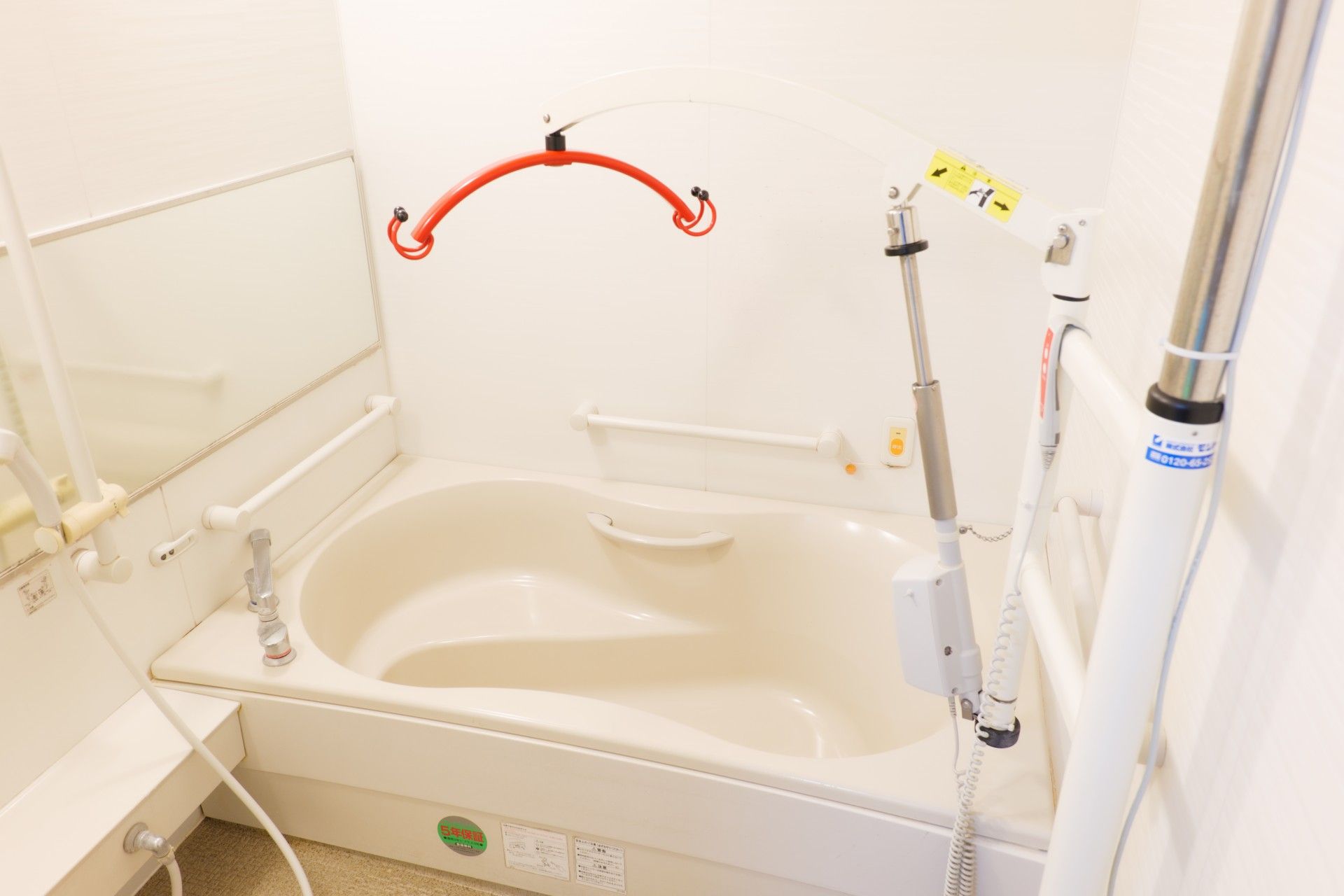 呼び出しボタンが付いた一人用の浴槽。白と赤のリフトが設置されている。