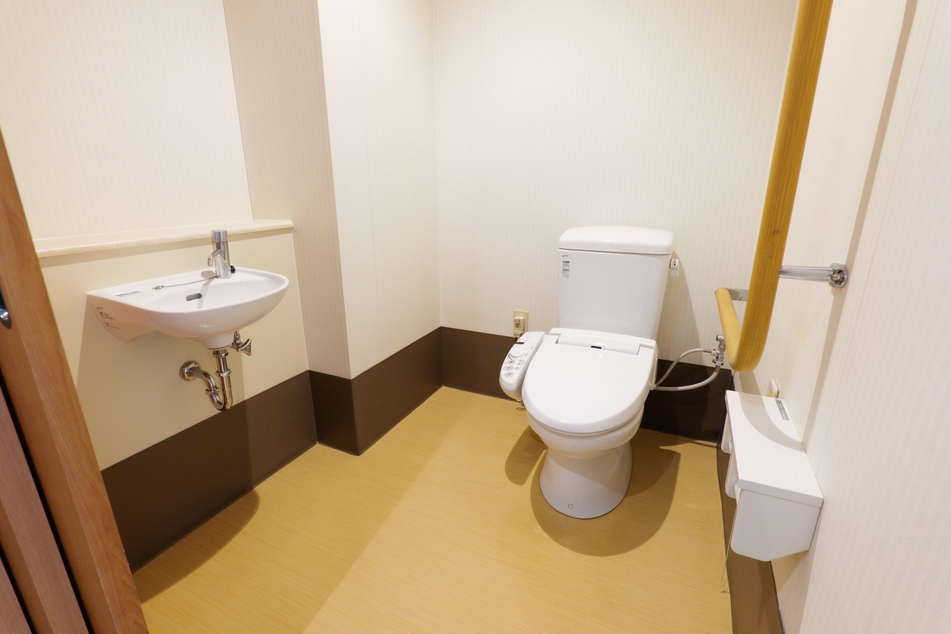 白い壁には呼び出しボタンとエル字型の手すりが付き、温水便座付きのトイレが設置されている。