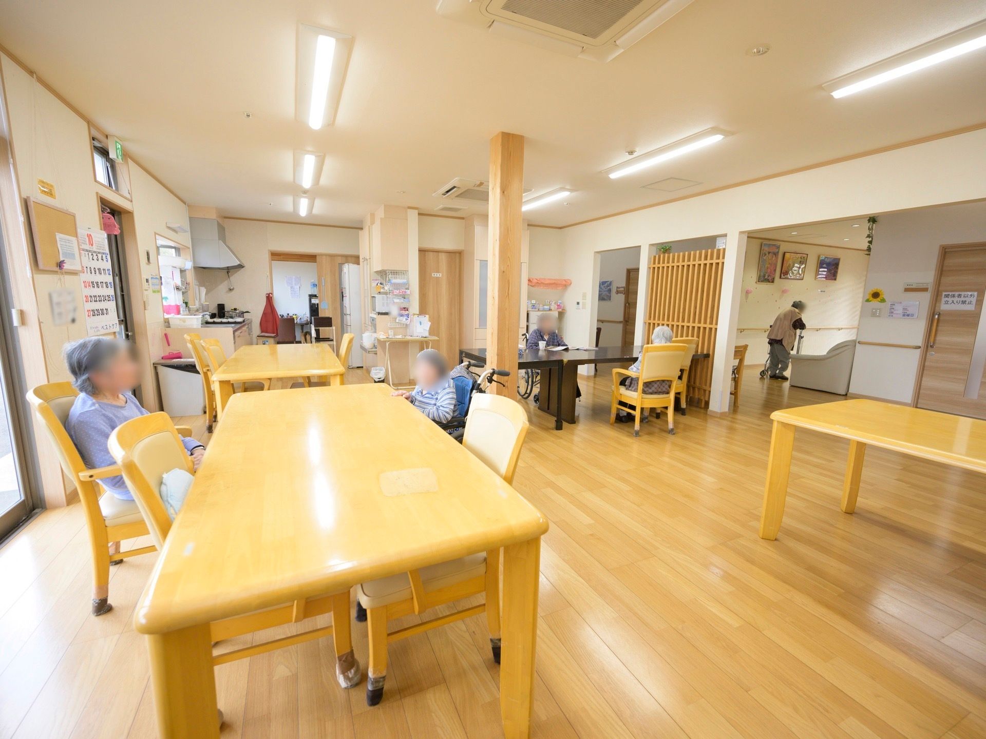 キッチンが併設されているダイニングで、数人の入居者様が椅子に座って寛いでいる。床は木目調のフローリングとなっている。