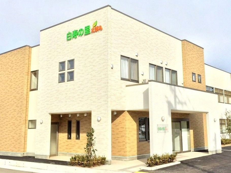 2階建ての建物はベージュ系で玄関には屋根が付き、花壇も設置されている。