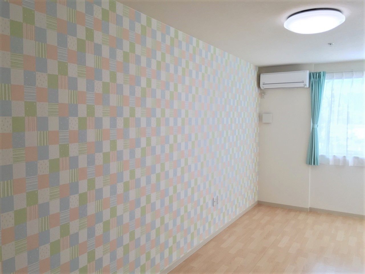 エアコンが付いたフローリングの居室。壁の一面はチェックの壁紙が貼られている。