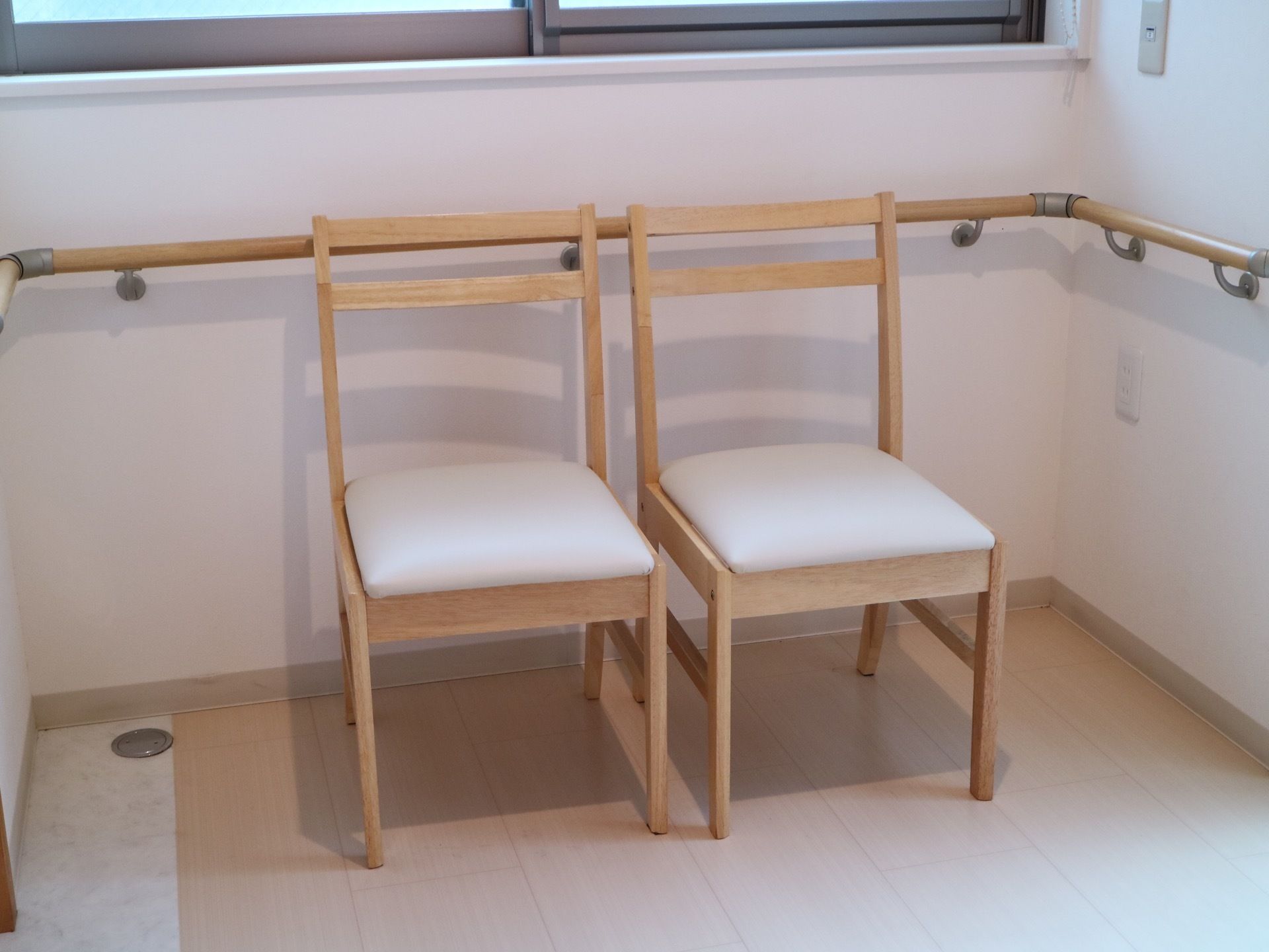 通路の一角に椅子が２脚置かれている。背もたれ付き。上部には窓が設置され、明るい日差しが降りそそいでいる。