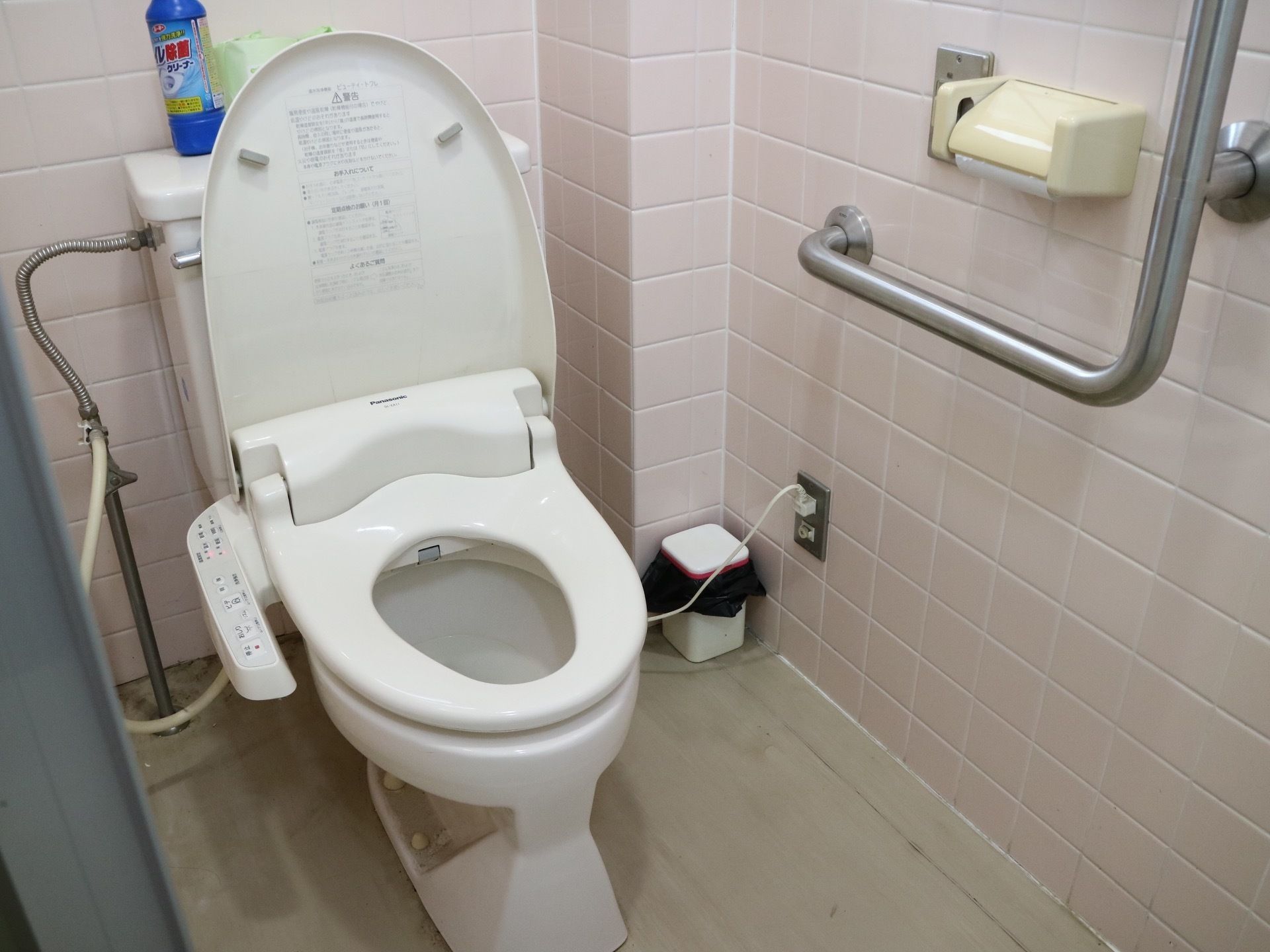 個室の洋式トイレで、温水洗浄機能付きの便座が採用されている。タイル張りの壁には、Ｌ字型の手すりがある。