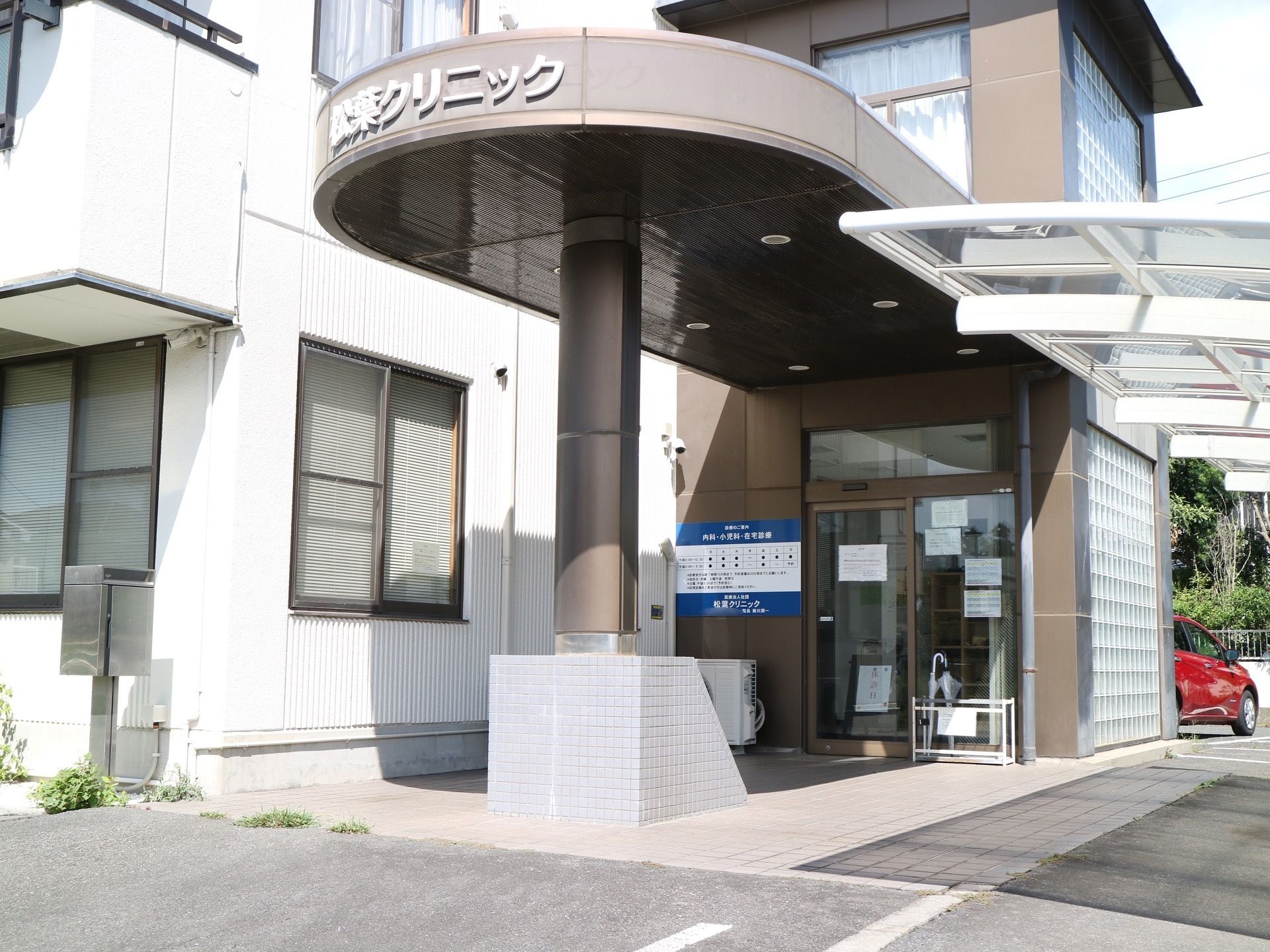 屋根の付きの車寄せが設けられている玄関である。自動ドア前には、傘立てやエアコンの室外機が置かれている。