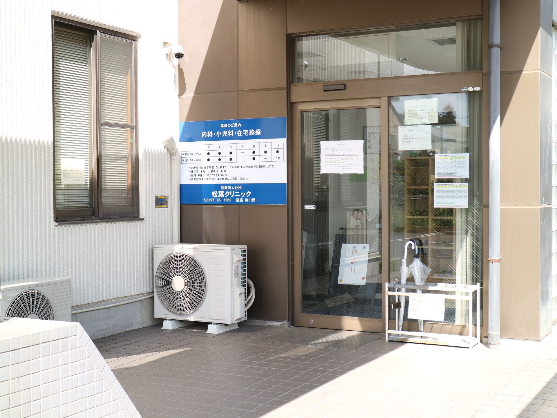 エアコンの室外機や傘立てが置かれている、エントランス付近