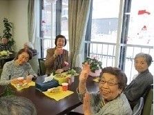 テーブルを囲む４名の女性入居者。テーブルの上にはカラフルなカップや軽食が置かれている。