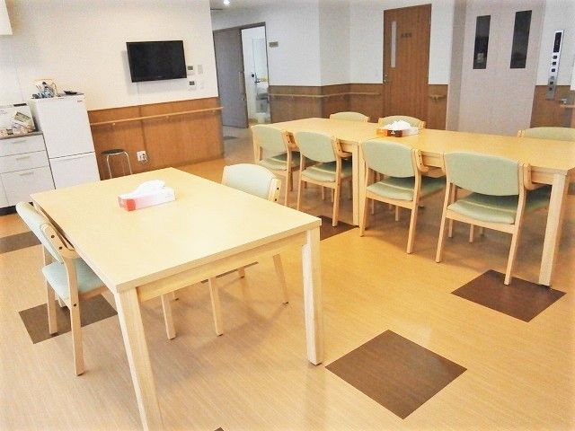木製のテーブルには椅子がセットされ、テーブルの上にはティッシュが置かれ、壁にはテレビもある。