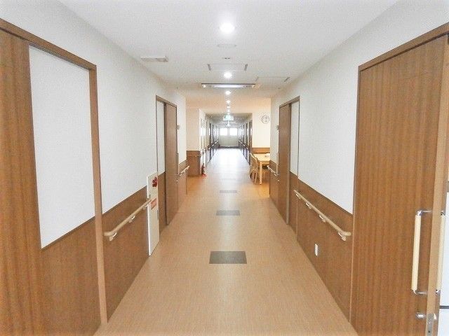 両サイドに手すりと居室のドアが並んだ廊下。中央に共有スペースのテーブルがあるのが見える。