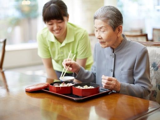 ご利用者がお食事をしている様子、それを見守る女性スタッフ