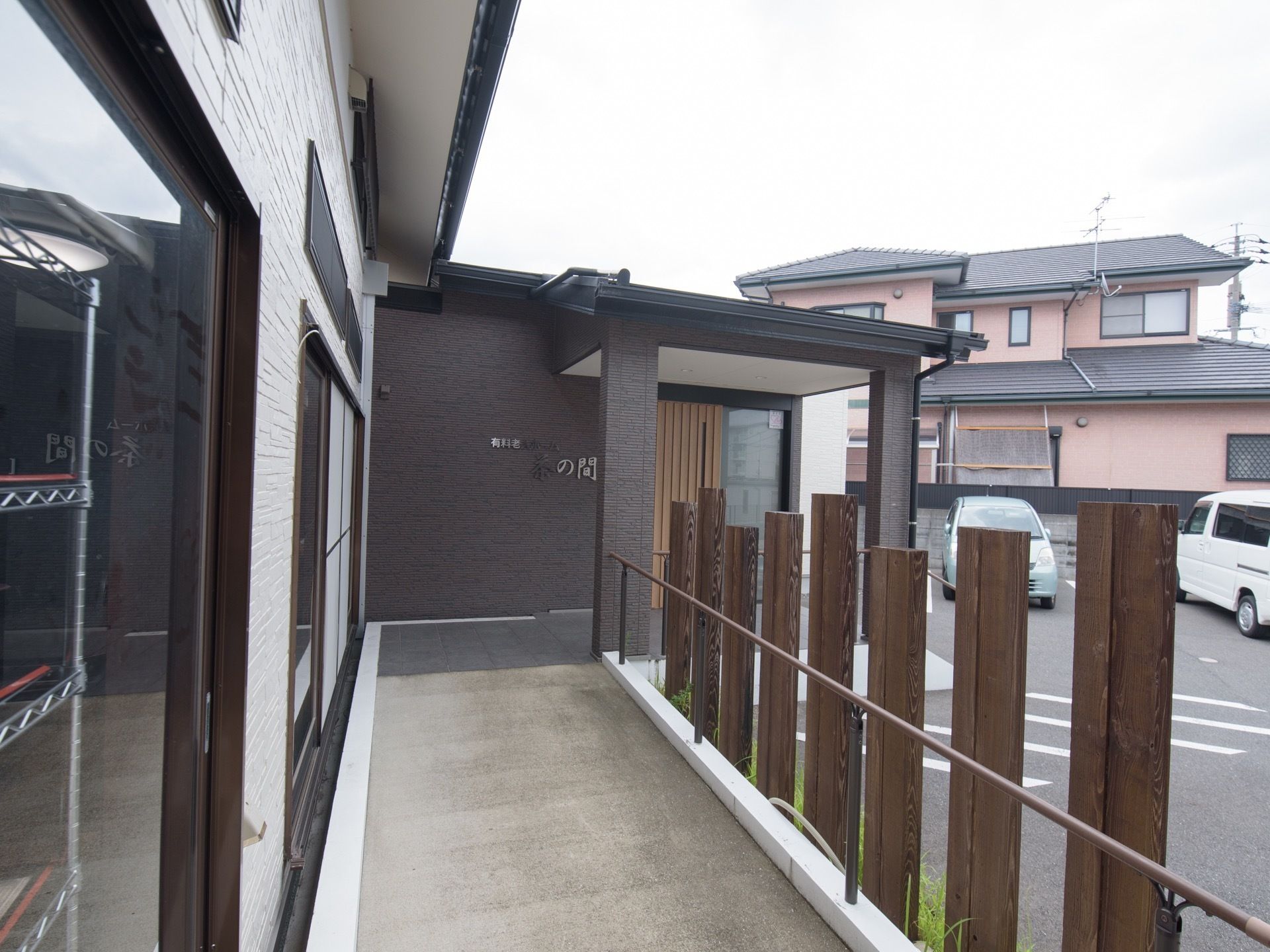 施設入口に傾斜が緩やかなスロープが設けられており、サイドには手すりがある。駐車場には、複数台の車が停められている。