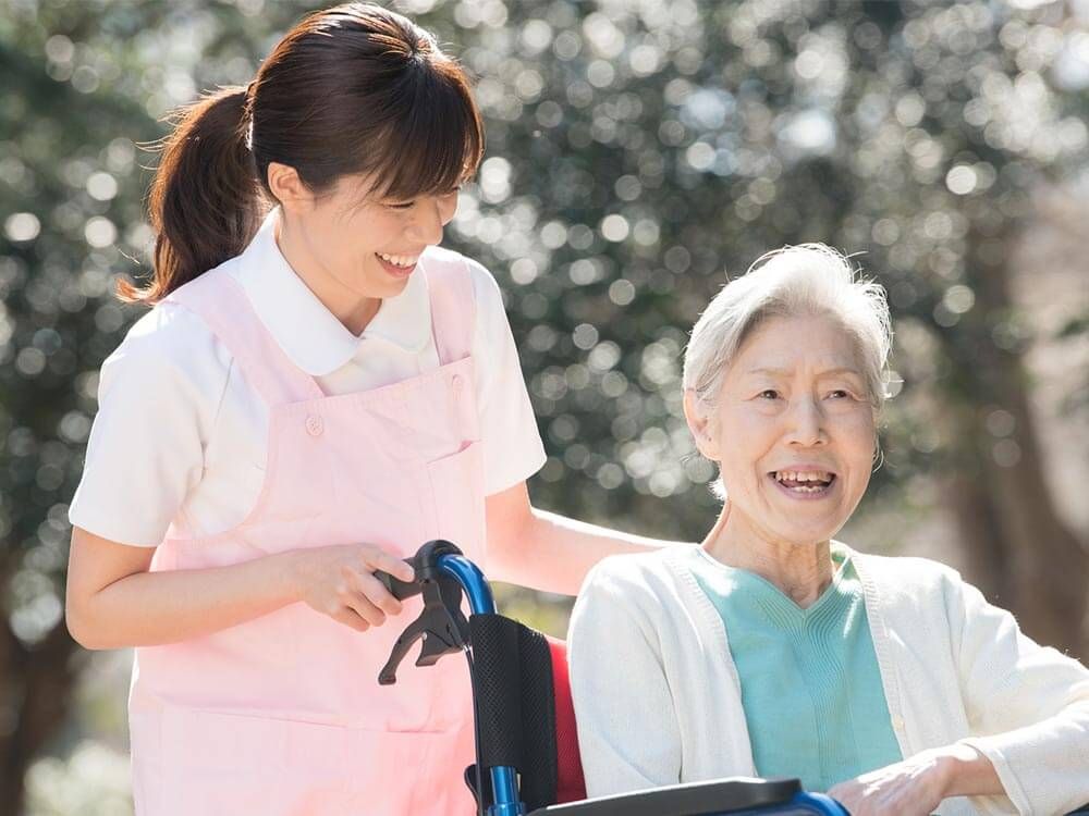 車椅子に座っている高齢女性と笑顔で介助をする女性ヘルパー