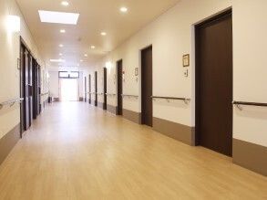 両サイドには手すりや居室のドアが設置されたまっすぐな廊下。突き当りには大きな度があり陽の光が入っている。ドアの隣には小さなフレームが付いている。