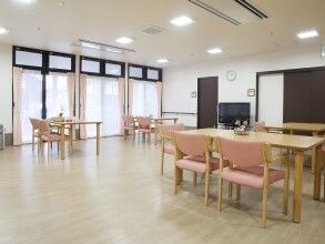 ピンクの椅子がセットされた木製のダイニングテーブルセットが複数並んだ食堂は、大きな窓がたくさんつき、明るい雰囲気。窓にはカーテンがついている。