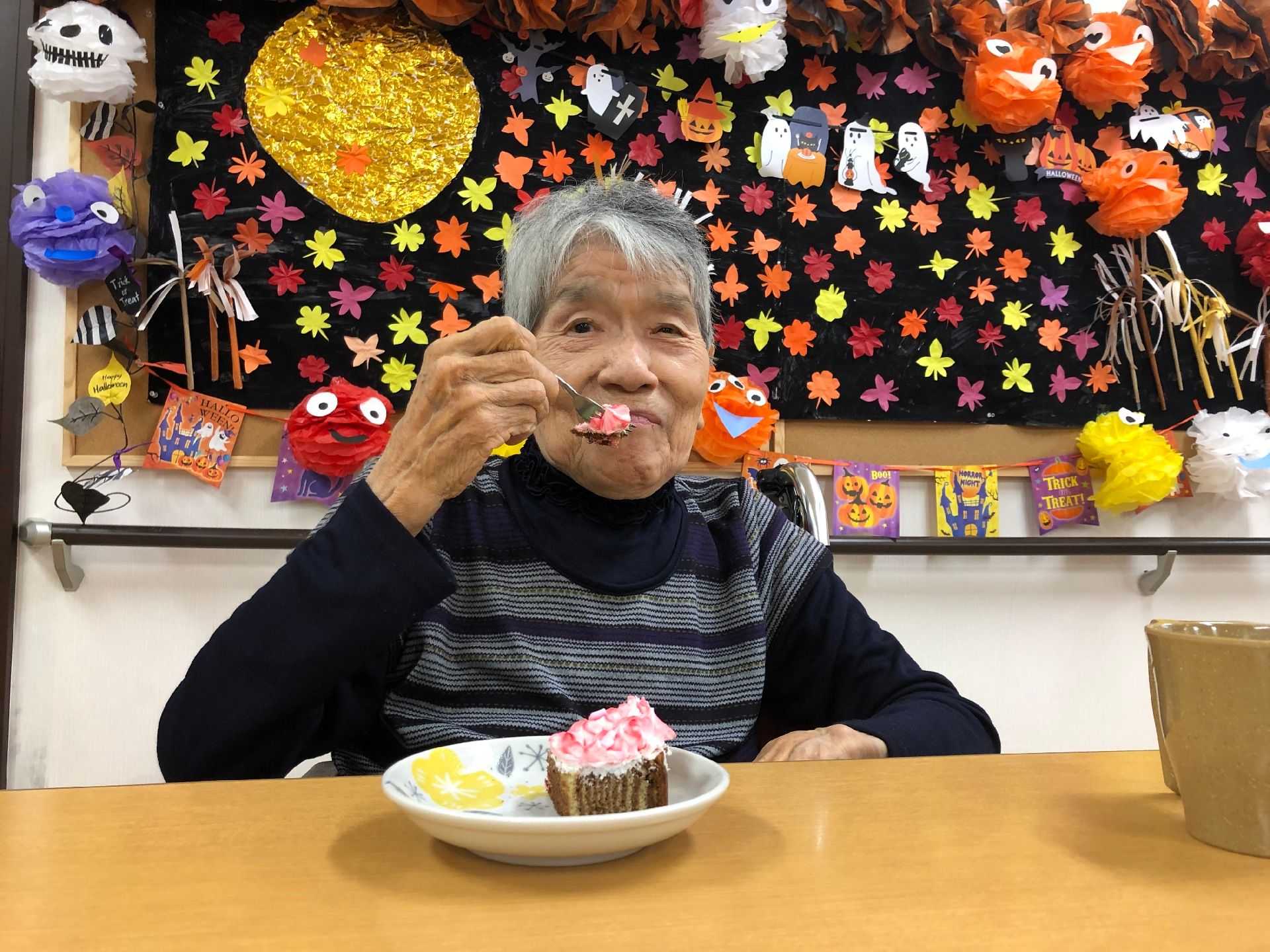 ハロウィンの飾り付けがされた部屋でおやつを食べる高齢者