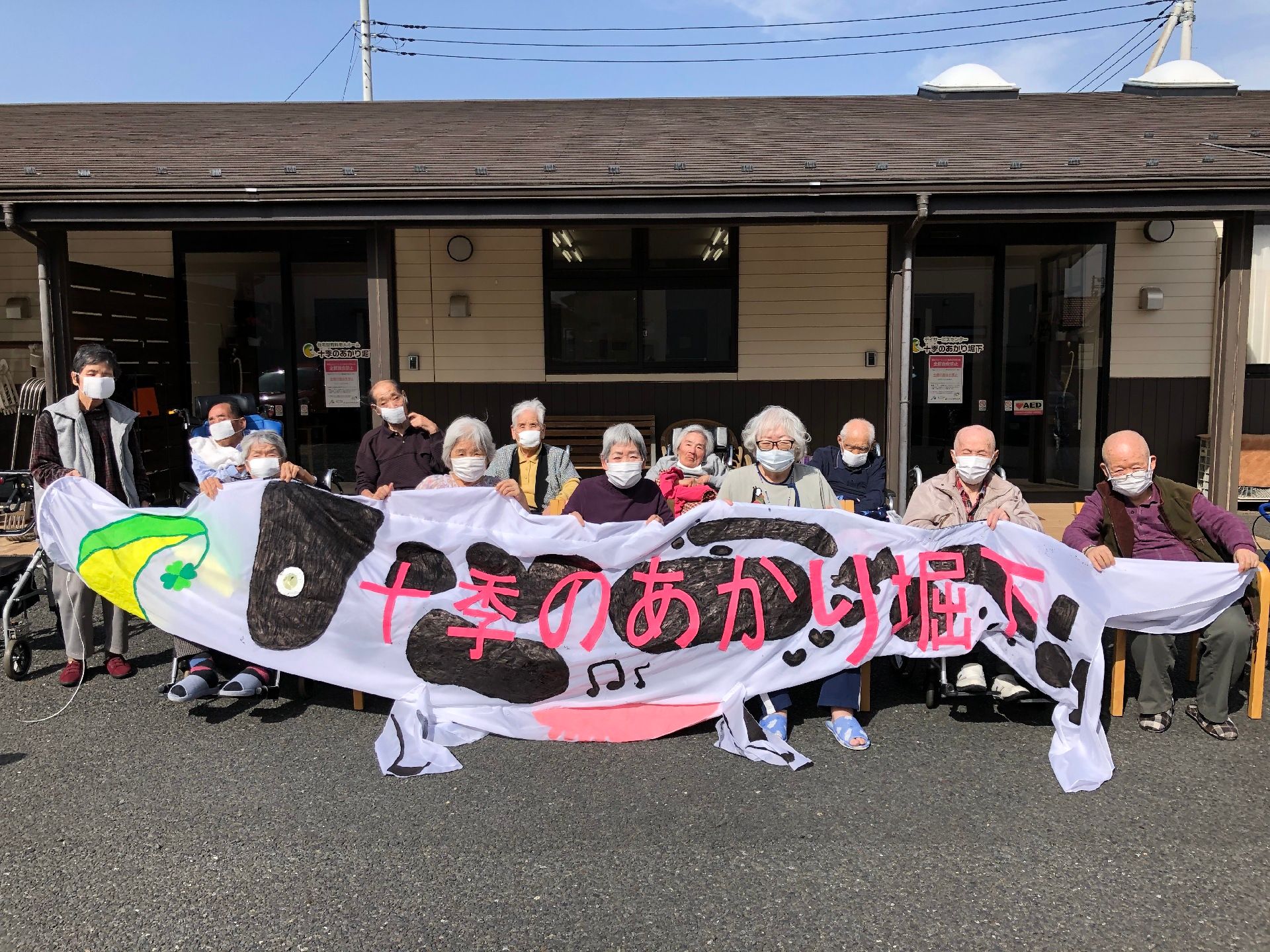 建物の前でマスクをして集合している高齢者とスタッフ