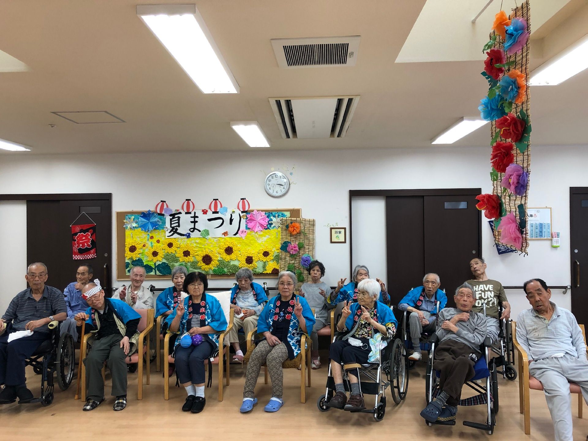 カーテンが付いた大きな窓がたくさんある明るい食堂。ピンクの椅子がセットされた木製のダイニングテーブルセットが複数置かれ、大きなテレビもある。